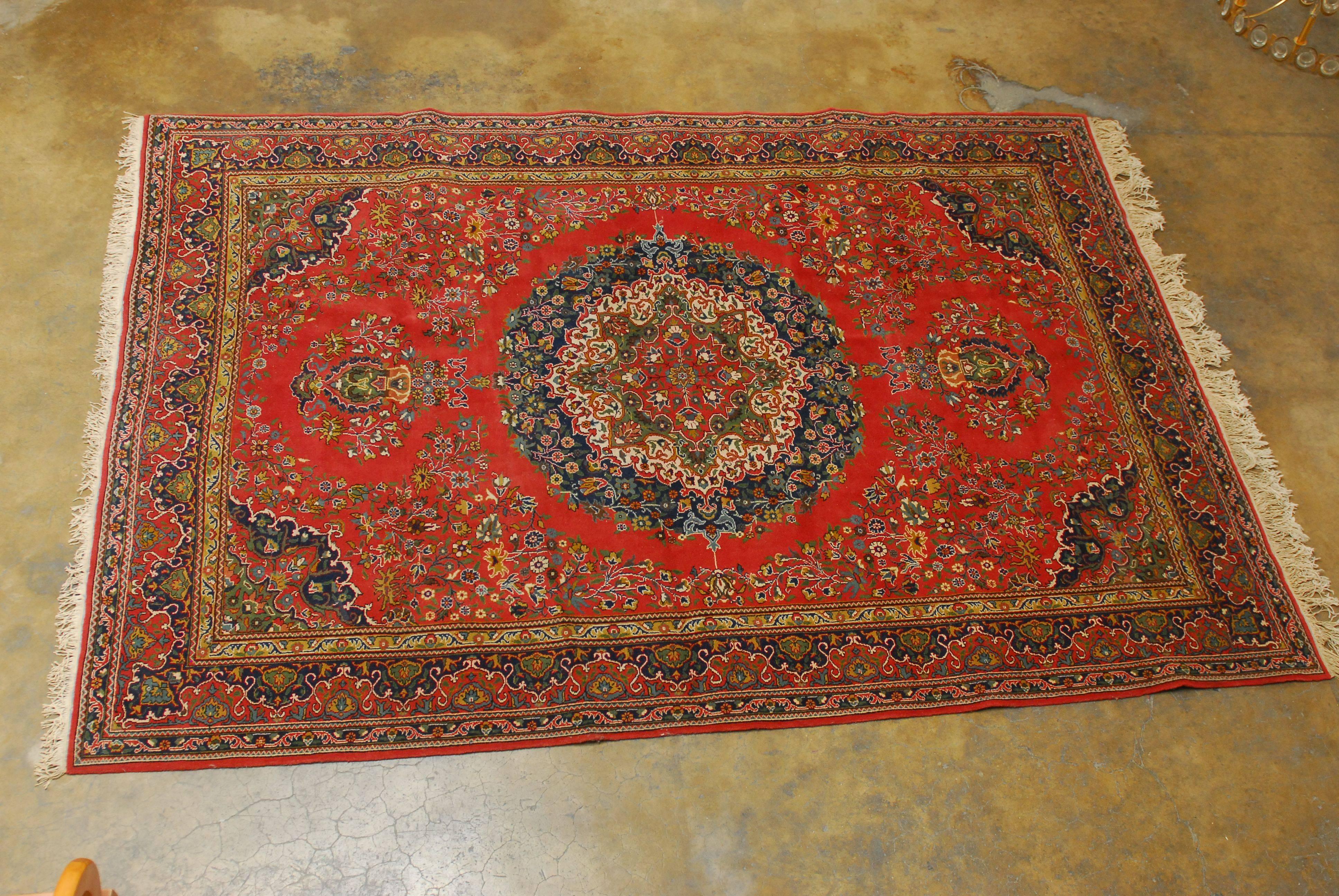 This beautiful Turkish rug has a formal central medallion in deep indigo blue and cream with intricate floral patterns over a crimson background. The field is also heavily adorned with floral vines and the carpet has a multi-band border.
