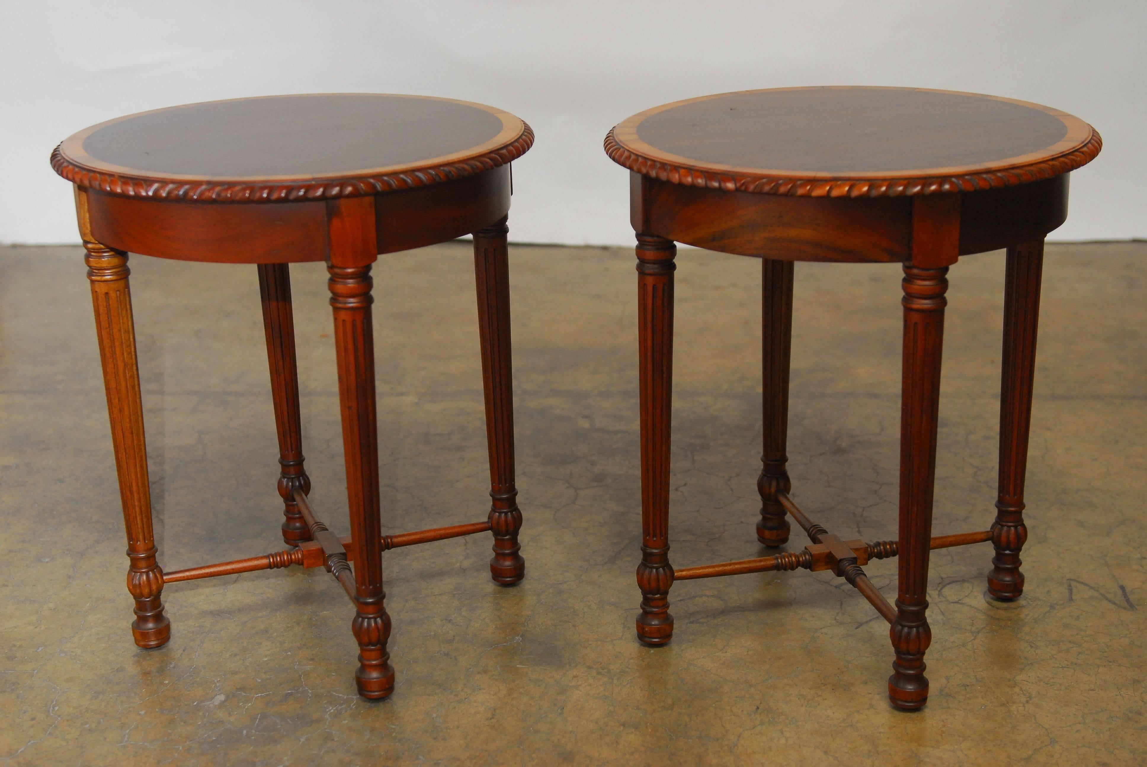Exquisite pair of round hand-carved mahogany side tables featuring a gadrooned round edge and contrasting mahogany inlay. Supported by four reeded tapering legs and conjoined by a turned cross stretcher. Impressive quality and workmanship. Perfect