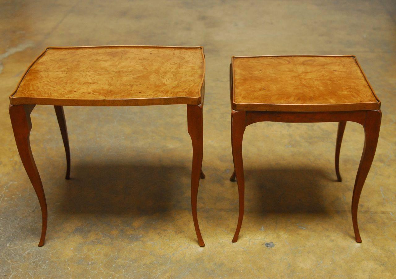 Elegant set of nesting tables by Baker featuring a rich burl wood galleried top with a serpentine edge. Supported by angular tapering cabriole legs.
