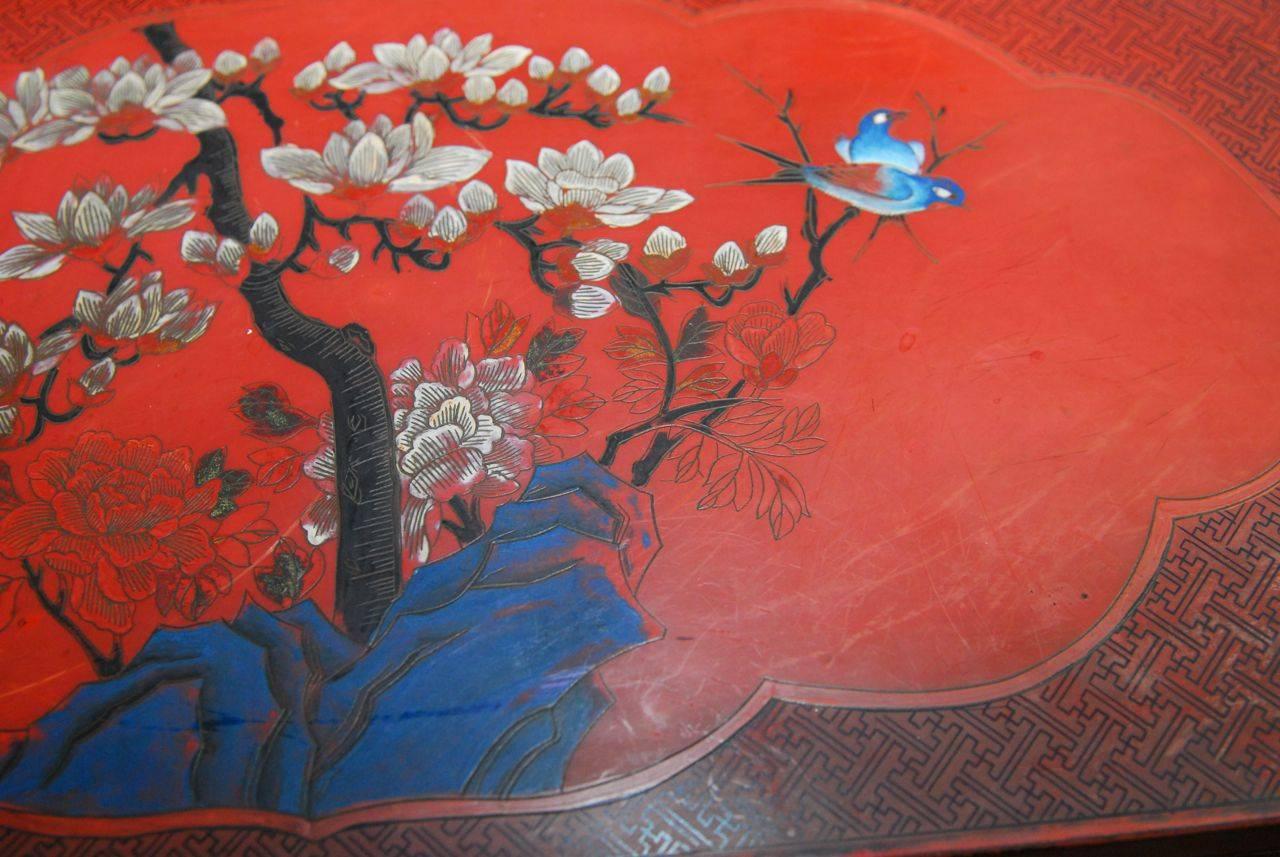 Pair of matching Chinese cabinets decorated with floral scenes and birds over a fretwork pattern red lacquer background. Each cabinet is fronted by double doors with brass hardware and lock plates and opens to a storage area with a hidden false