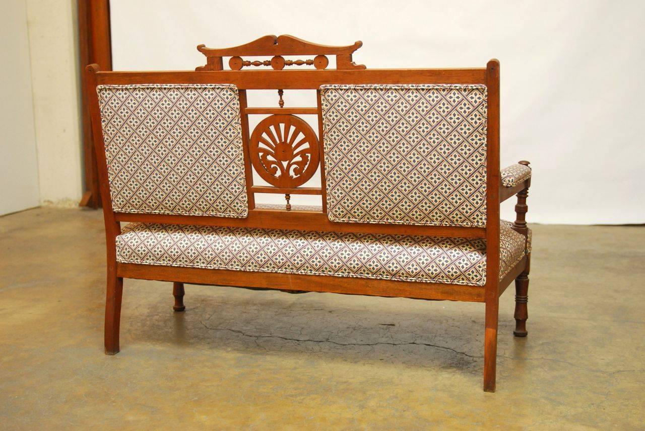 Distinctive American Eastlake settee featuring a carved medallion and a detailed crown back support. Supported by turned legs and arms. Upholstered in a red, white, and blue geometric pattern fabric with a double welt border that compliments the