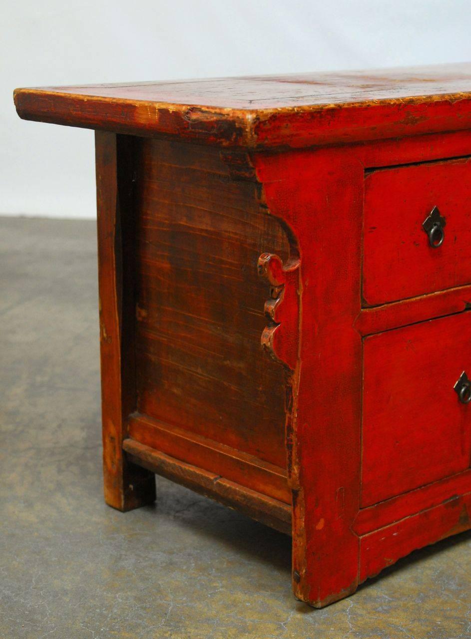 Long Chinese wooden buffet featuring a red lacquer finish. Fronted by four drawers and storage doors. Mortise and tenon joinery throughout with a well worn top panel and decorative scrolled sides. Lots of character on the vintage patina with wear