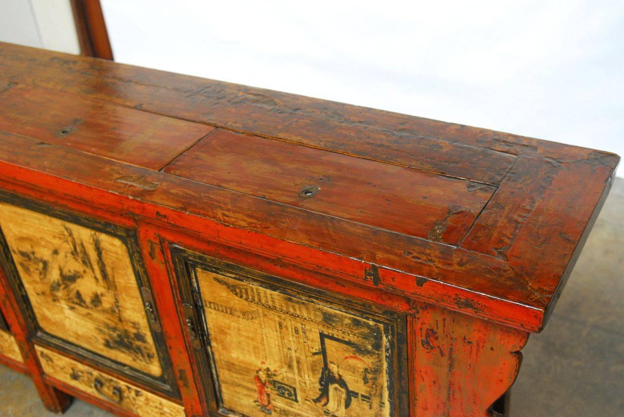 Large Chinese altar sideboard featuring a hand-painted lacquer finish with Asian scenes on the three front doors. This elongated side table has two shelves inside each door and three drawers along the bottom. The top of the buffet has three rare