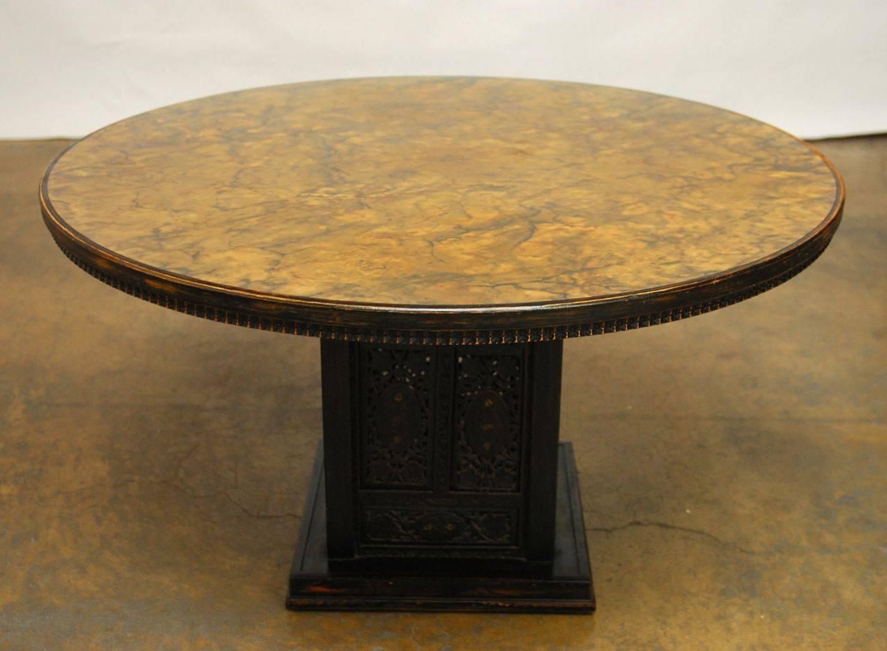 Aesthetic round dining table featuring an Anglo-Indian carved square base with an ebonized finish. This rare and unusual table was produced by Ritts of California and has a beautiful faux marble top. It features a distressed finish and intricate