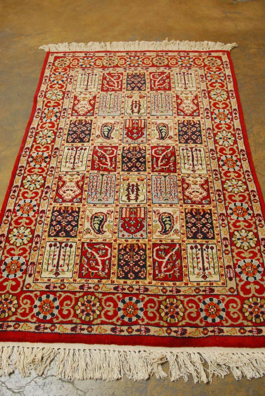 Baktiari style carpet made in India of hand-knotted wool pile. Intricate geometric patterns and symbols over a red ground with vibrant colors and a soft, thick pile.
