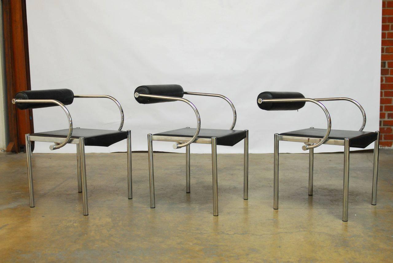 Chic set of dining chairs made in the manner of Ludwig Mies van der Rohe with round tubular chrome frames and upholstered in black Naugahyde. The seat pads have a faux leather finish and stitch detail on the sides. Sleek profile with a curved arm