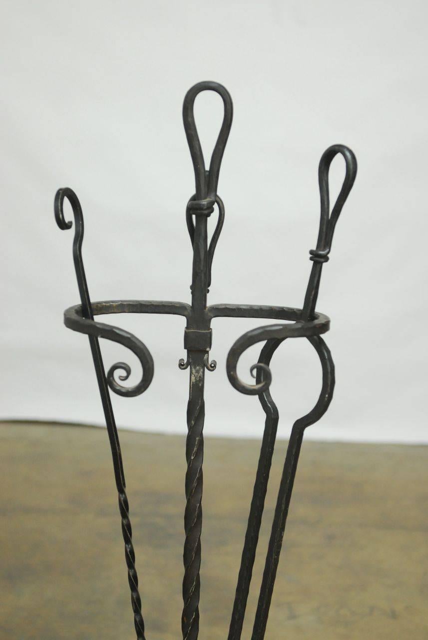 Giant fireplace tool set with stand made of wrought iron with scrolled arms and legs. Set includes brush, tong, and poker. No shovel. The stand has a twisted column support and the arms have been beveled with small facets to further decorate the