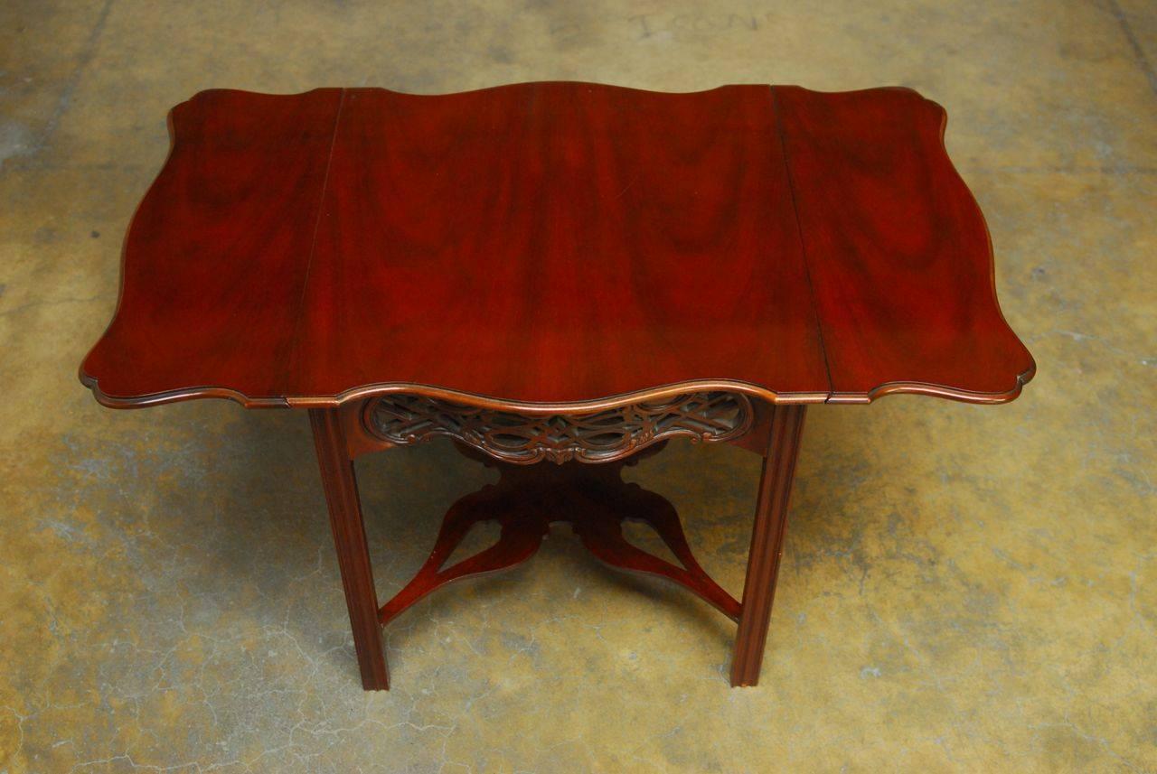 Distinctive tea table by Baker constructed of mahogany and made in the Chinese chippendale taste. Featuring drop leaf sides and a serpentine top with intricately carved open fretwork frieze. Supported by straight chamfered legs and joined by