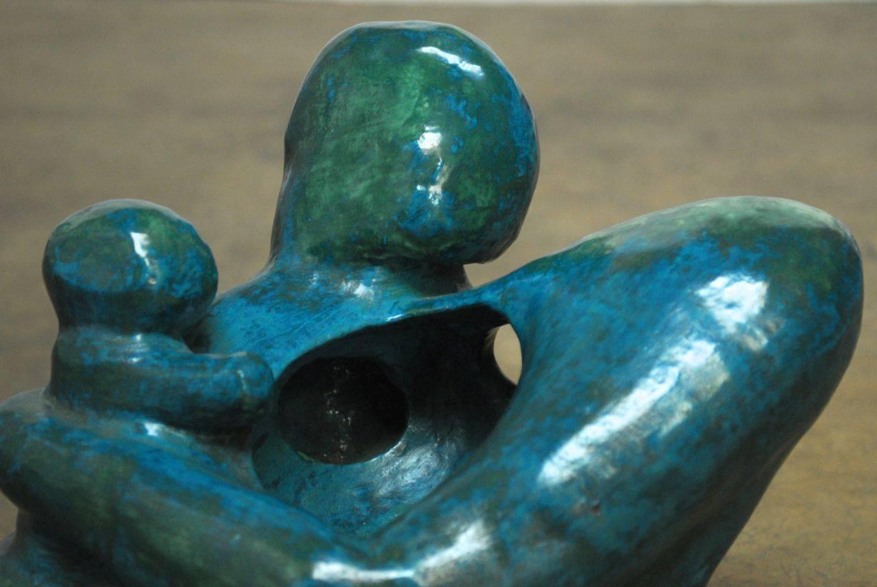 Stunning abstract sculpture of a human form embracing an infant. Deep blue and green glazed ceramic finish with fascinating movement from all angles. Sits on a Lucite base. The sculpture has the feel of patinated metal and is very substantial.
