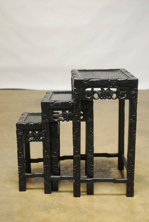 Beautiful hand-carved nesting tables made in Hong Kong by George Zee. Featuring an ebonized finish with a grape and vine motif. Supported by square carved legs with hump-back stretchers. Makers mark plaque on bottom. 
