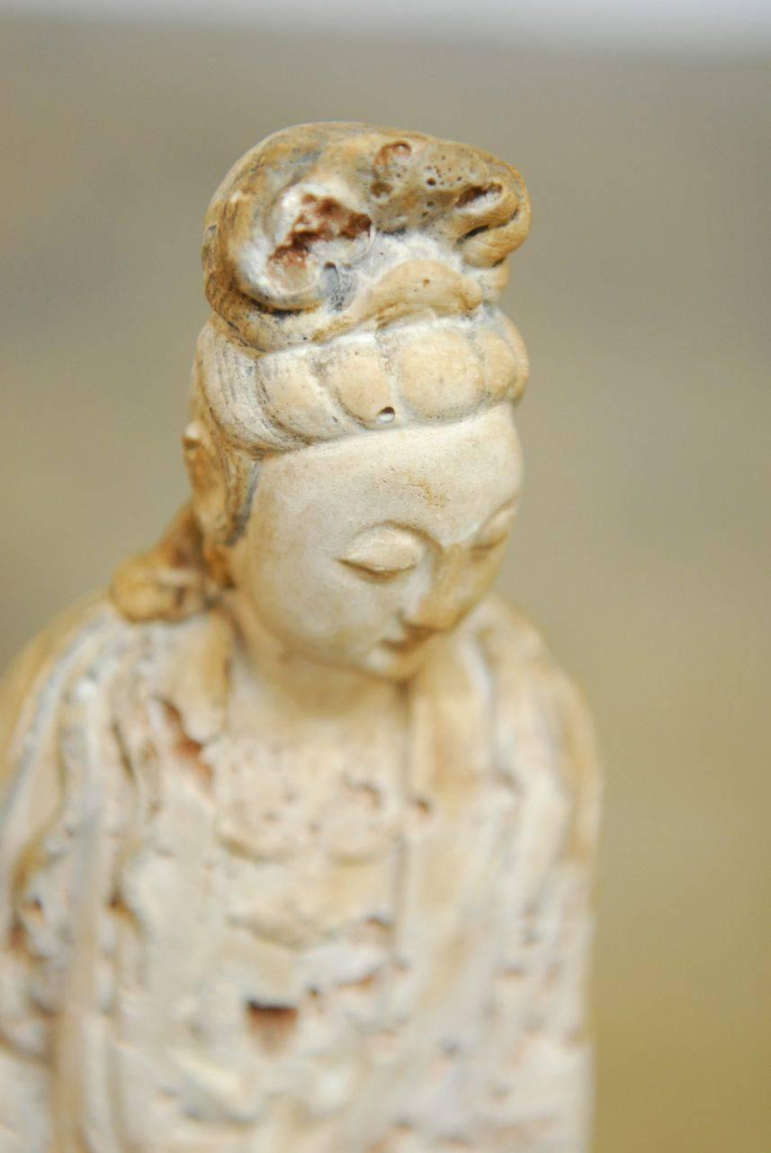 Goddess of mercy Guanyin sculpture standing on a base holding a basket. Made of a composite stone material with an intricate aged patina. Haunting face and beautiful flowing robe with a light terra cotta stone like finish.
