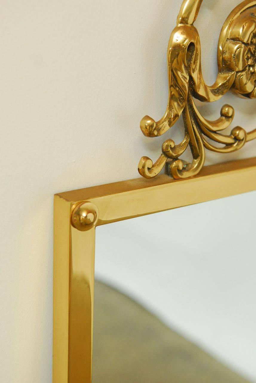 Lavish brass wall mirror from the Art Nouveau period featuring a stylized floral decorative scrolling top. Rectangular form frame with a polished finish. This heavy mirror shows superior craftsmanship from a bygone era.
