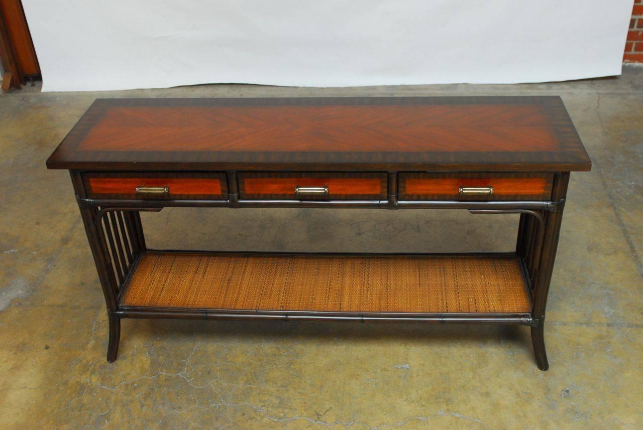 Handsome bamboo and rattan two-tier console table by Palacek of San Francisco, CA. Featuring a pole rattan frame and veneer marquetry top and drawers with decorative border. The console is fronted by three drawers with faux-bamboo brass pulls and