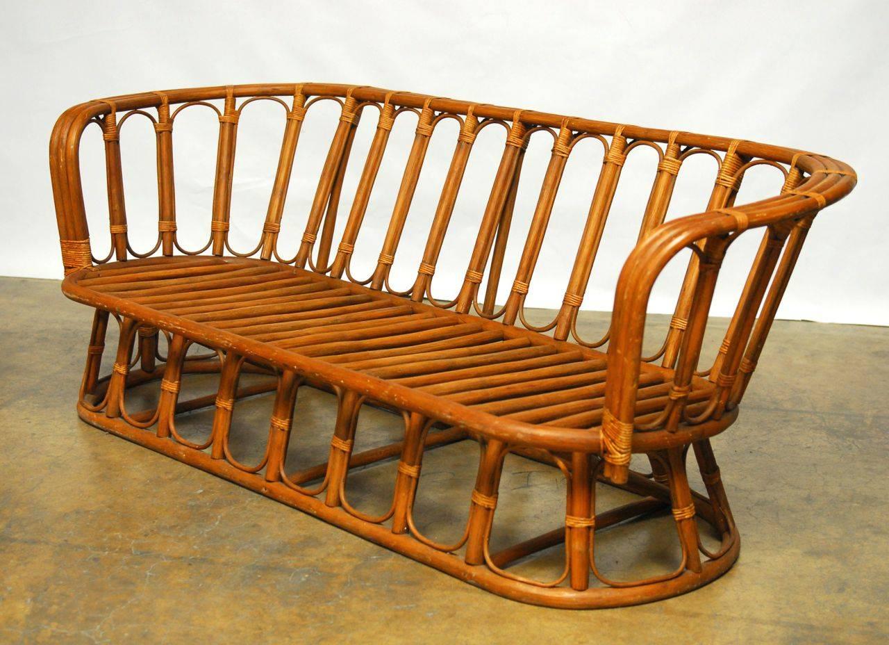 Fantastic bamboo rattan settee features a stunning series of architectural inspired loops forming arches throughout the top and base of the sofa. Handmade of dark rattan in Montpellier, France. This is a piece of quality and elegance with wide arms