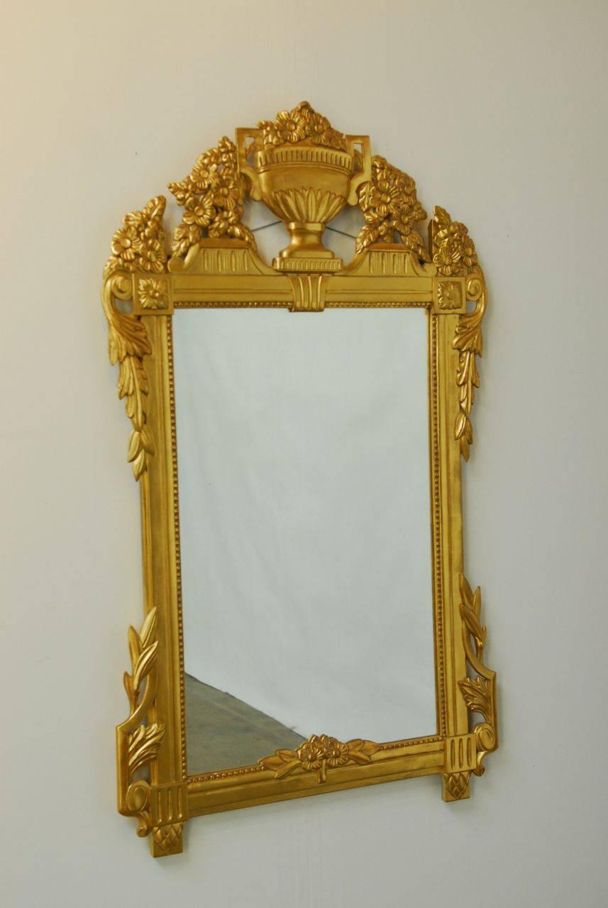 Remarkable French Regency gilt wall mirror made in the Louis XVI taste featuring a large sculpted urn form at the top. Beautiful bouquets of carved flowers and acanthus leaves are depicted on the top and sides. There are rosettes in the top corners