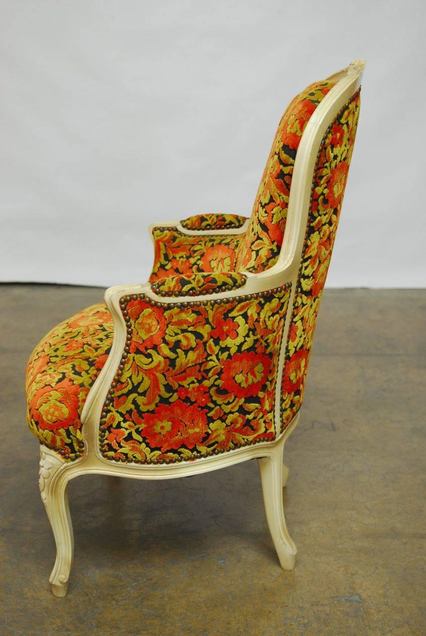 Stylish French armchair professionally upholstered in a bright velvet floral pattern with brass nail head trim. Features a hand-carved frame with a cream colored lacquer finish and intricate floral details. Supported by cabriole legs with curved