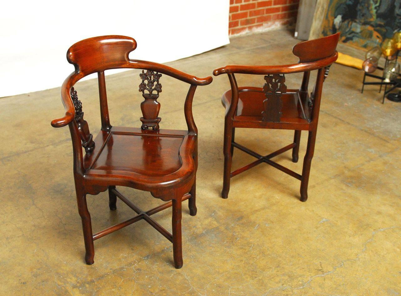 Pair of extremely finely carved rosewood armchairs, likely hongmu, featuring stunning iridescent grain. Horseshoe backs cradle well carved floral arrangements in vases, supported by offset legs and cross stretchers. One of the finest examples of