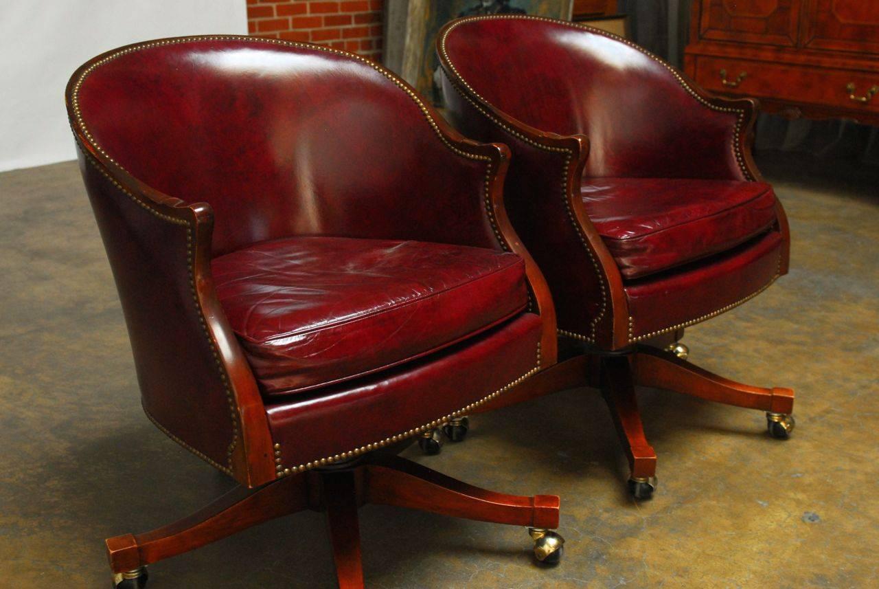 Gorgeous smooth burgundy leather with brass nailhead trim featuring a barrel back form made of solid mahogany. Luxurious rolling desk chairs that are supremely comfortable and refined. Available singly or as a pair.