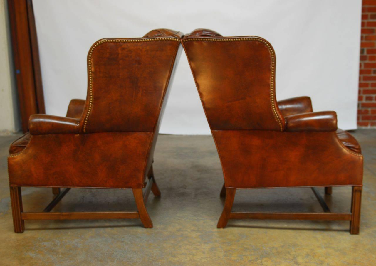 Classic pair of wing back chairs made in the Chippendale manner. Produced by Schafer Brothers in marbled brown leather with brass nail head tack trim. Large, fully developed wings with a lovely profile. Supported by square mahogany chamfered legs.