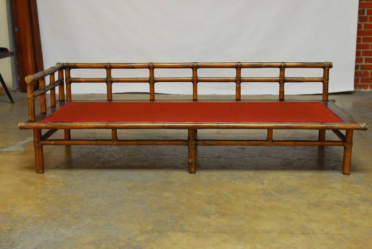 Distinctive bamboo daybed constructed in the Chinese style by McGuire of San Francisco, CA. Featuring an open fretwork bamboo back. Reinforced with rawhide strapping throughout. The bed has a wood platform with a spring padded bottom covered in red