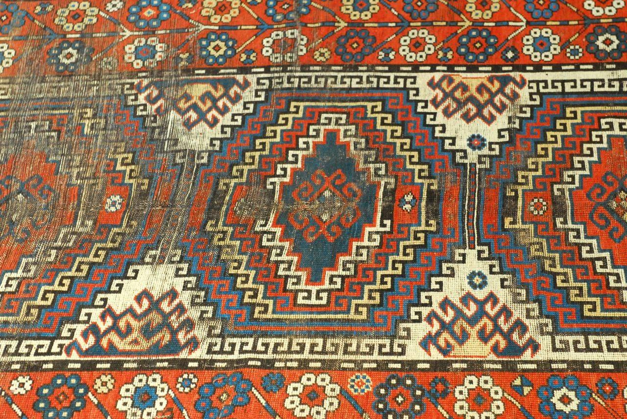 Impressive traditional Caucasian rug from the Kazak region featuring geometric designs and stylized floral patterns on the border. Strong vibrant blues over a distressed red ground. Shows just the right amount of aging, wear, and lovely patina.