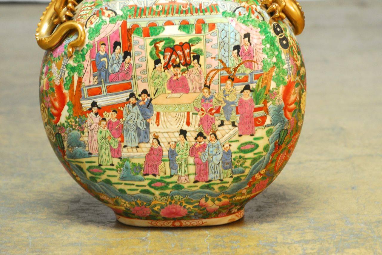 Large Chinese porcelain moon flask vase decorated with a famille rose array of colors depicting palace social scenes. Features two large applied gilt dragon handles flanking each side of the neck. Artist chop stamp on bottom.