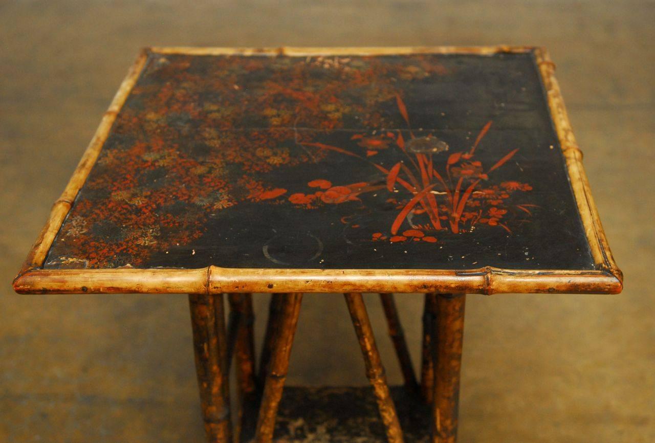 Rare, English lacquered table made of scorched bamboo in the chinoiserie taste. The top features a lacquer floral motif with a distressed finish. The bottom shelf has a lacquer floral design and the frame features decorative arched supports attached