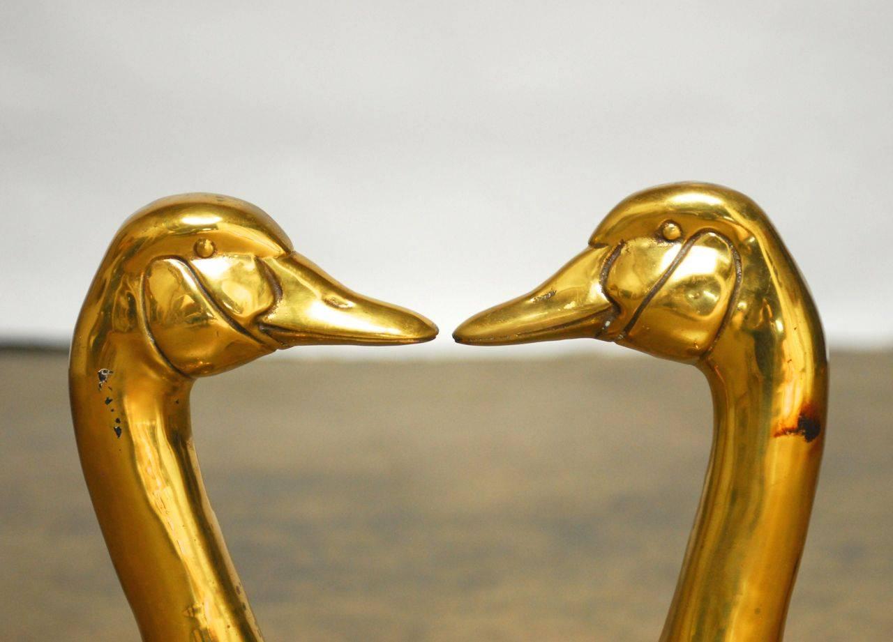 Distinctive duck goose figural andirons made of polished brass supported by delicate legs with ball feet. Large head and neck busts that demand your attention. Each in inscribed with the letter "H" on the front.