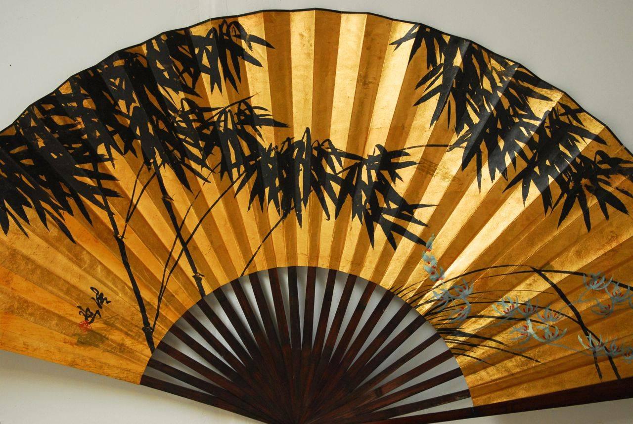 Large display piece, this fan features rosewood stained bamboo slats supporting a gilded painting of bamboo. Striking piece fits well into chinoiserie and Hollywood Regency decor, even as an original Japanese painting.