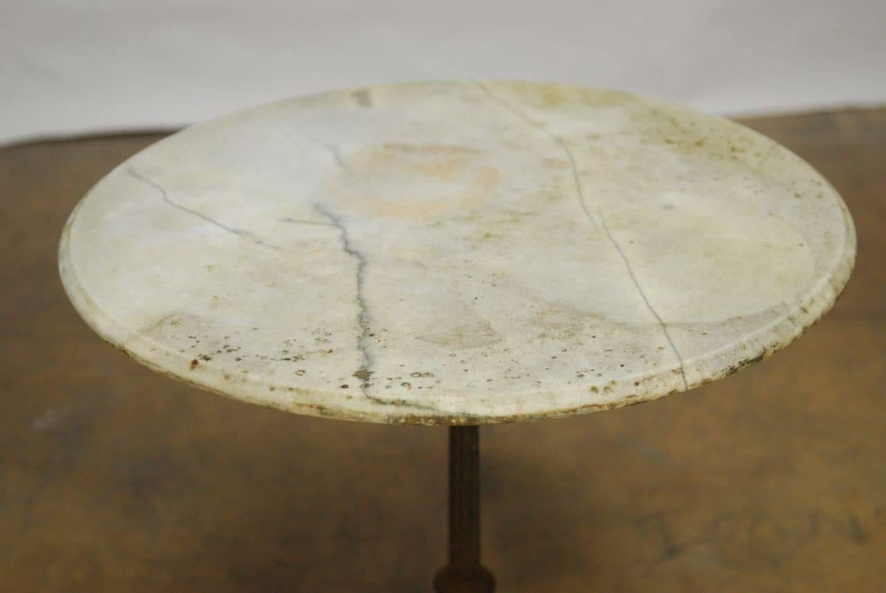 Turn of the century iron bistro cafe table featuring a weathered marble top. Lovely patinated finish on the iron base with an authentic Parisian outdoor look on the vintage marble.