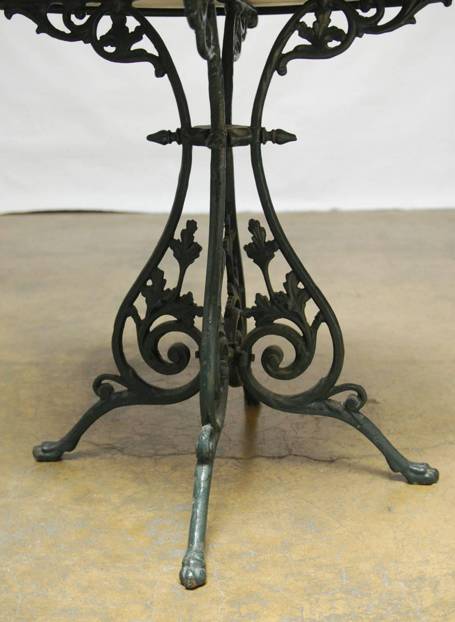 Stylish wrought iron bistro cafe table with a scrolling foliate leg design. Features a white marble round top with decorative notches on the rounded edge. Finished in a deep green lacquer with a vintage patina. Harmonious combination of marble and