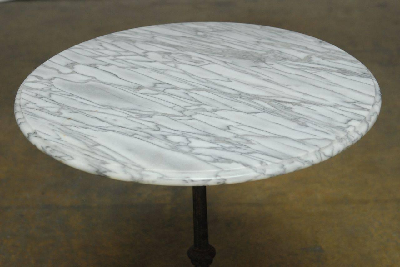 Delightful French iron bistro cafe table featuring a Carrara marble-top with an interesting grain pattern. Lovely detail on the tripod iron base with a patinated black finish.
