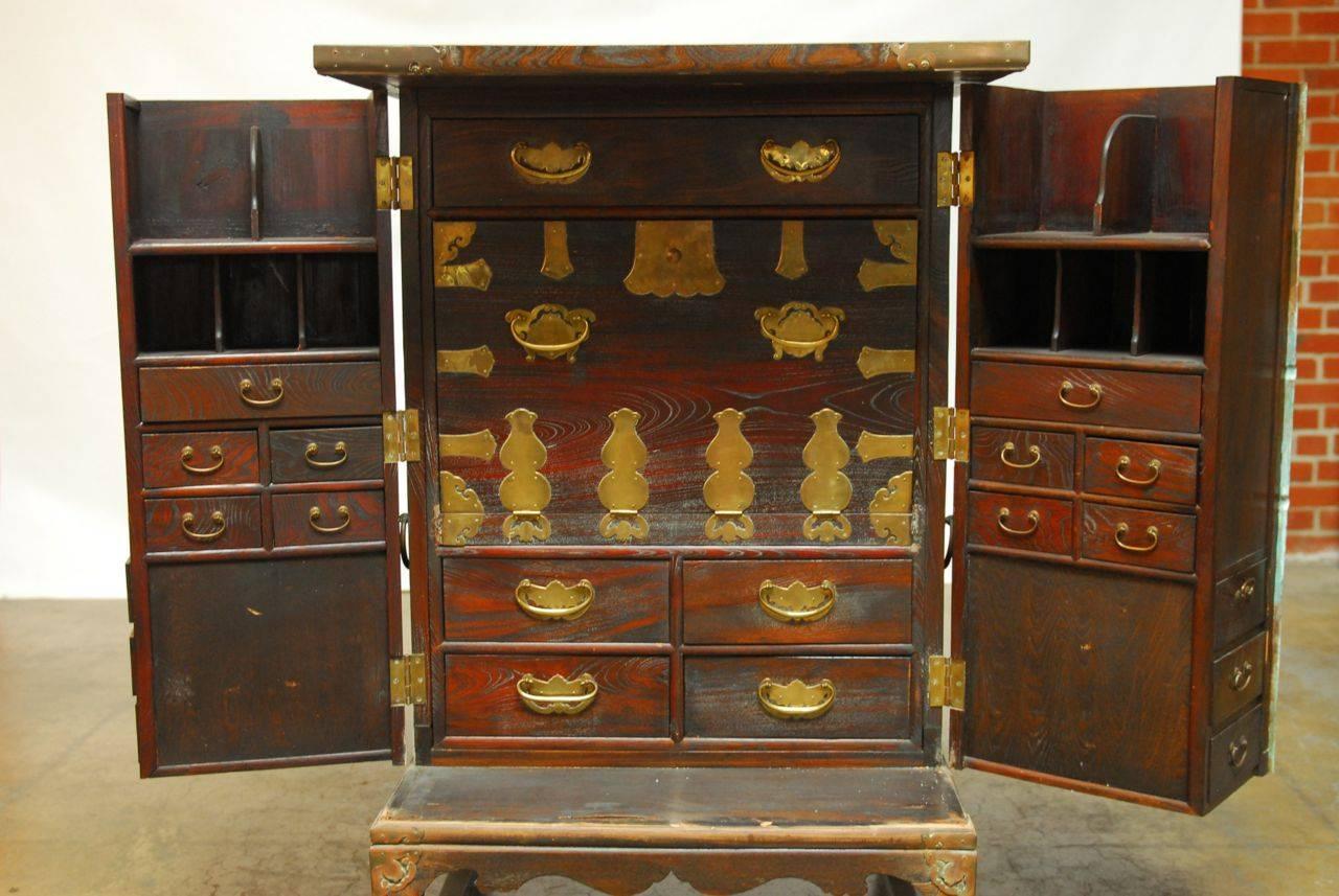 Impressive Asian campaign style cabinet featuring two large front doors that open to reveal a drop down writing desk and fitted with numerous storage drawers. Adorned with opulent brass hardware, hinges, and pulls. Rare Tansu styled chest