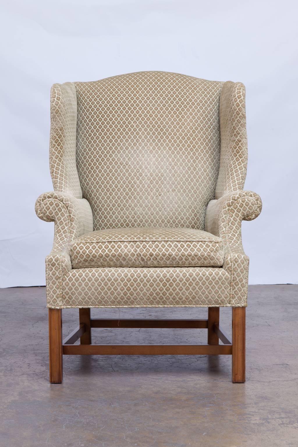 Generous traditional wingback chair by Baker featuring well developed serpentine arms and wings with a geometric pattern soft upholstery over a cream silk background. Supported by fluted front legs with an H-stretcher in excellent condition with no