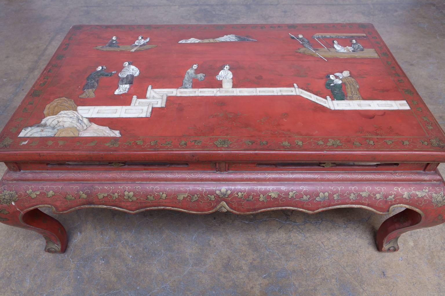 Stunning Chinese coffee table with a red lacquered finish featuring extensive gilt decoration and a carved hard stone top depicting people around a lake. Floating top panel with a pierced serpentine apron supported by cabriole legs. Lovely original