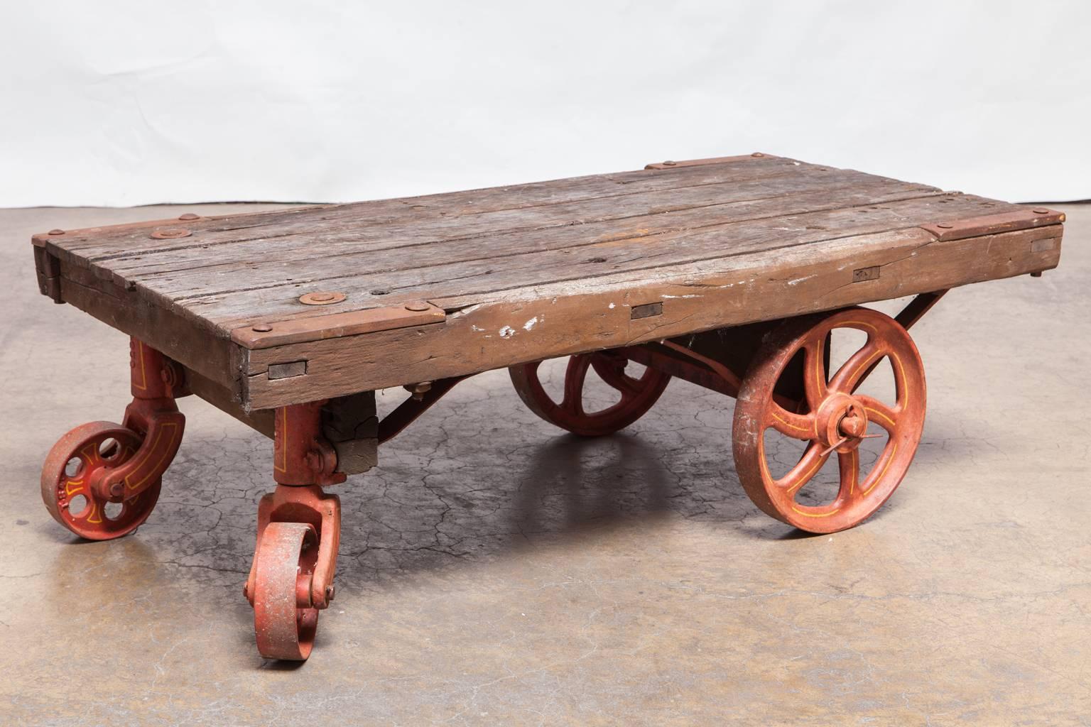 Charming Industrial rolling trolley cart with a wood plank top and featuring four cast iron wheels finished in red. Constructed with mortise and tenon joinery with heavy metal hardware. Level top makes it a great candidate for a coffee table.