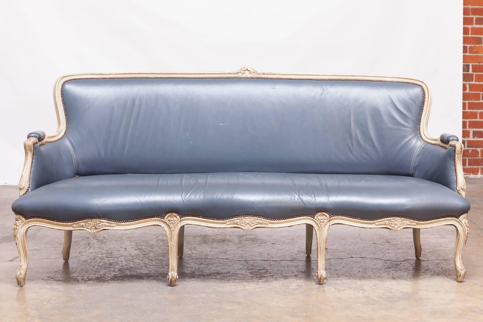 Stunning Louis XV style canapé sofa upholstered for William Gaylord in a French blue leather. Lovely painted frame with a distressed finish and accented by brass nail head trim. Rare serpentine seat supported by eight cabriole legs in the front and