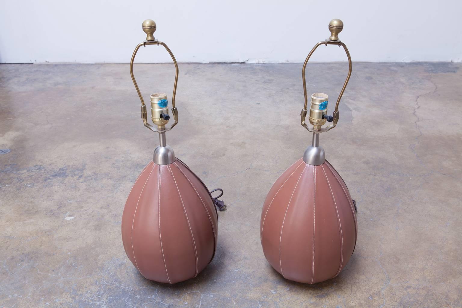 Rare designer lamps featuring top grade leather stitched covers over melon shaped bodies. Topped by brushed nickel covers and brass hardware with finials. No shades included.