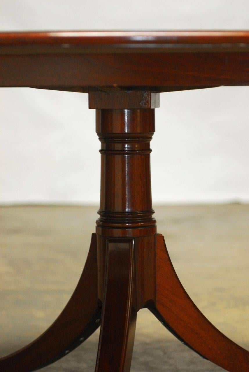 Impressive round breakfast dining table featuring a mahogany top banded in satinwood. The table is supported by a thick pedestal with three sweeping legs ending in brass toe protectors and casters. Made in the George III taste by Kindel Furniture