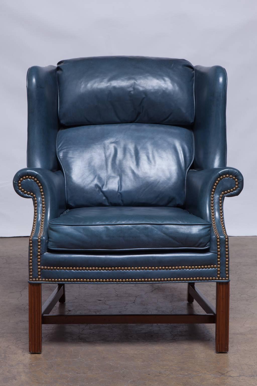 Classic wingback chair with matching ottoman made by Schafer Brothers in the Chippendale style with a mahogany frame. Featuring rich leather upholstery finished in a regal French blue with brass nail head trim accents. Supported by chamfered legs