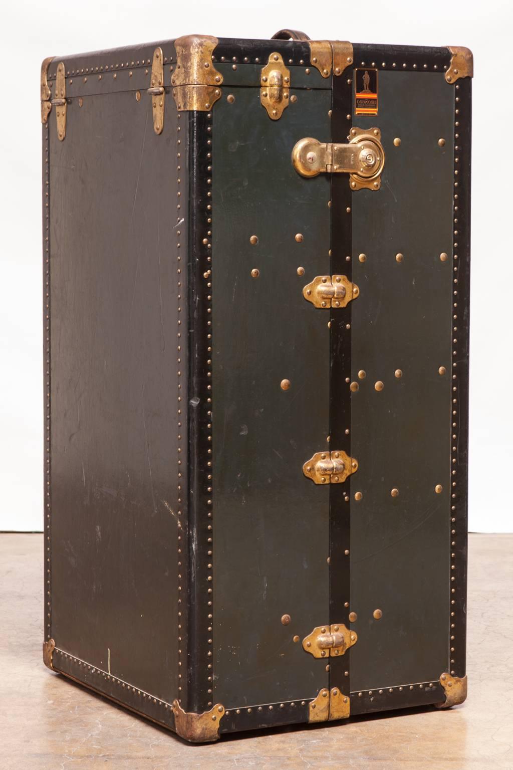 Exceptional wardrobe steamer trunk made by Oshkosh. Features a navy blue vulcanized fiber exterior with black trim and brass hardware. Excellent condition given age and use with a shiny patina. Rare investment quality trunk from one of the top five