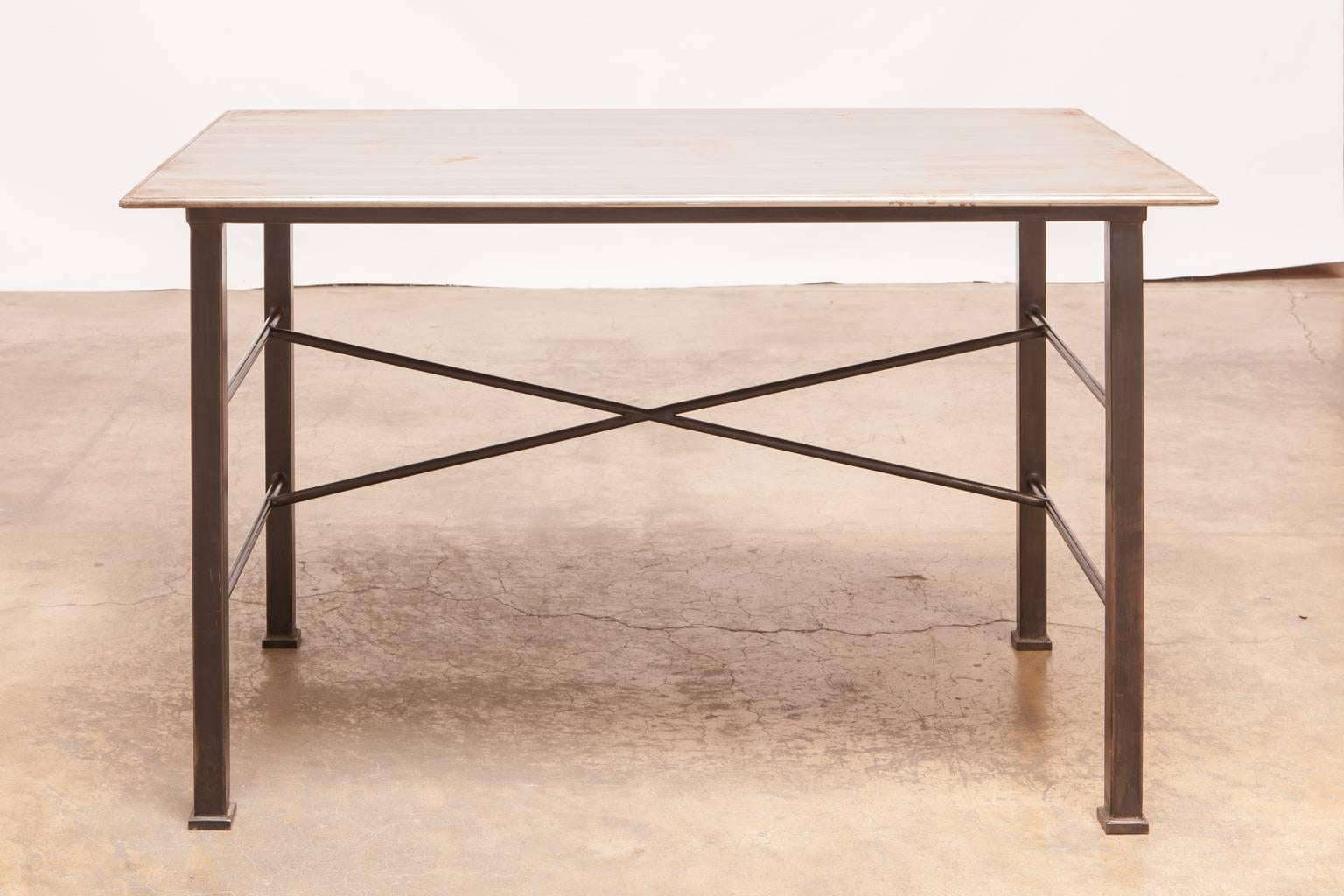 Fine modern Industrial desk constructed of steel featuring a patinated rectangular top supported by large square legs and conjoined by round stretchers. The bottom of the work table is finished in a black patina and sits on square feet. The desk top
