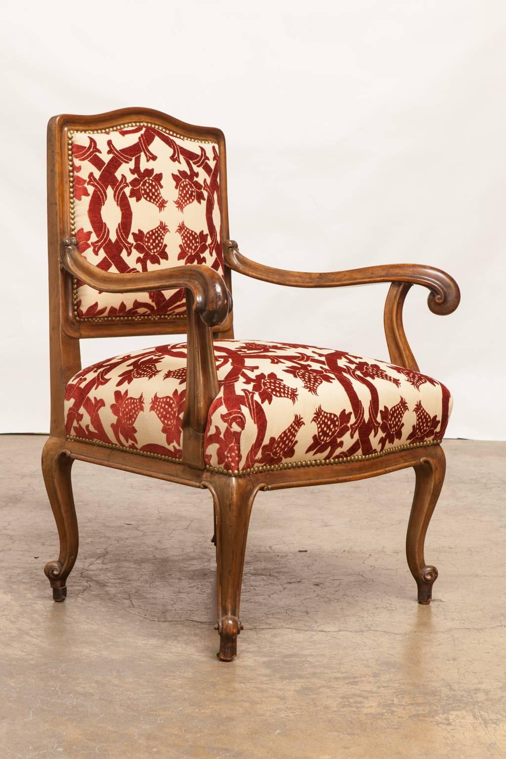 Unique carved Rococo style armchair featuring long, graceful scrolled arms and a square back. Newly upholstered with a burgundy floral and vine pattern over a cream ground. Accented with brass nail head trim and supported by cabriole legs with