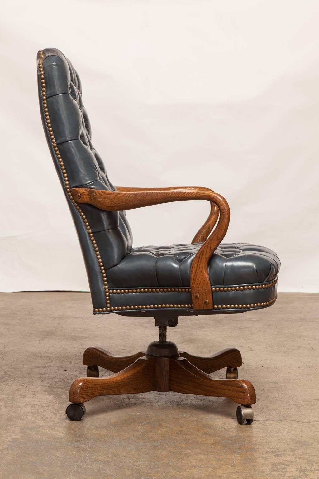 Impressive executive desk chair featuring a French blue tufted leather upholstery and accented by brass nail head trim. Produced by Schafer Bros. with soft, pliable leather in excellent condition. Supported by a wooden base on casters. Matching