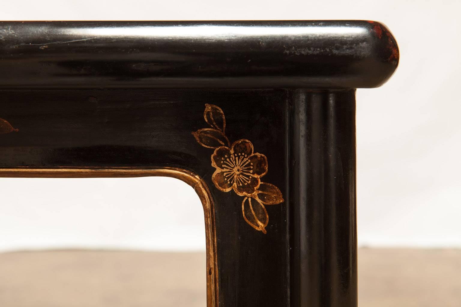 Charming black lacquer pedestal table or Chinese stool decorated with gilt floral embellishments and butterflies. Supported by round legs with elongated spandrels on each leg joined on each side that terminate at the box stretchers.