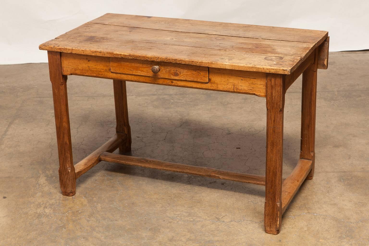 Rustic French country pine dining table that has two leaves and a fold down panel in the rear. Featuring soft, worn wood with an aged patina. Fronted by one drawer with a wooden pull and supported by square chamfered legs with rounded stretchers.
