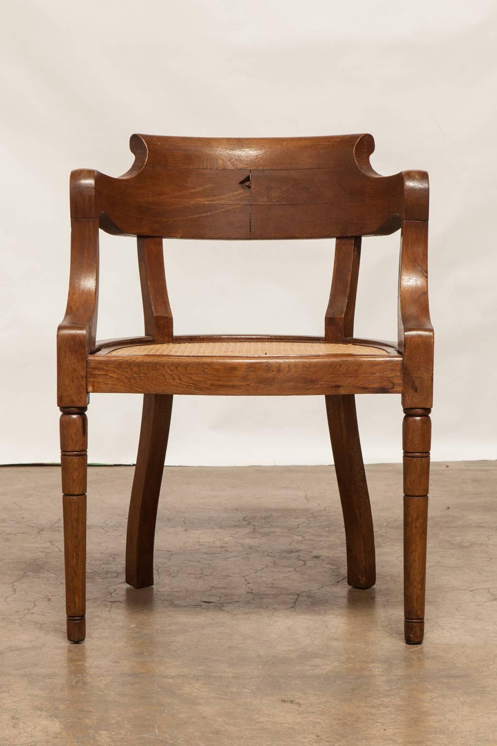 Handsome French carved armchair made in the Louis Philippe taste featuring a caned seat. Thick, carved oak frame with graceful curved arms and supported by pillar shaped turned legs.