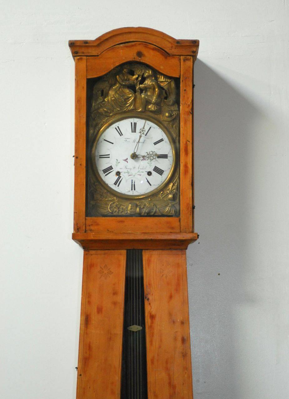 Country French pine Morbier or comtoise long case clock featuring an impressive brass repousse surrounding the enamel dial. Classic French potbellied case housing a freestanding weight-driven pendulum. Known as an eight day clock with two key holes