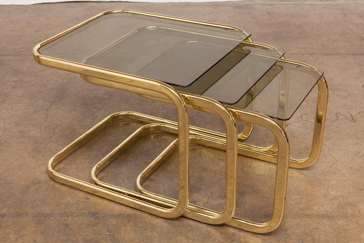 Striking set of three brass and smoked glass nesting tables attributed to Milo Baughman for DIA. Constructed from brass plated steel with smooth, sleek frames and each featuring a plate of dark tinted glass. Classic Mid-Century design excited in a