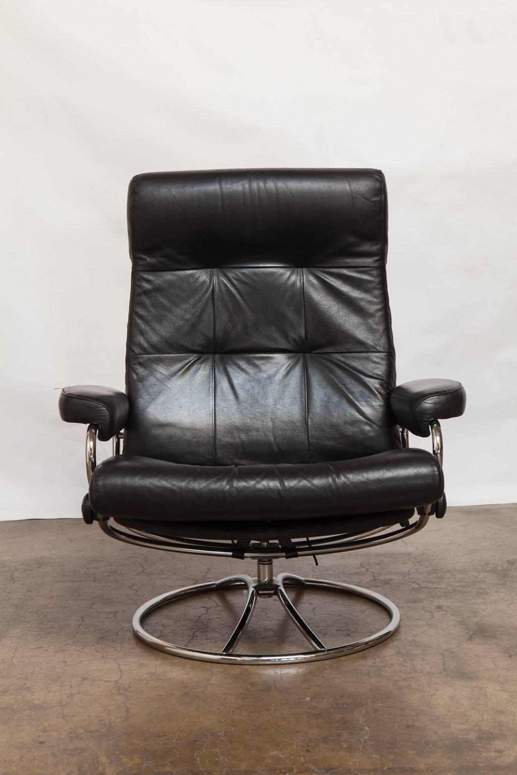 Mid-Cenury Modern Ekornes stressless black leather reclining lounge chair and ottoman featuring a chrome frame. Stressless recliners are made by Ekornes in Norway and are the finest recliners made. The chair has a unique glide system that follows